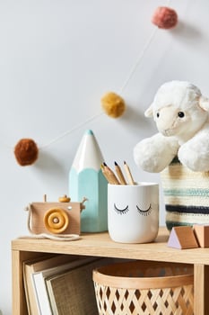 Stylish scandinavian newborn baby room with toys, plush animal, photo camera and child accessories. Cozy decoration and hanging cotton balls on the white wall
