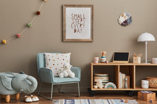 Cozy interior of child room with mint armchair, brown mock up poster frame, toys, teddy bear, decoration and hanging cotton colorful balls. Beige wall. Warm kid space. Template. photo