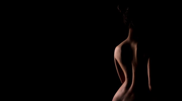 The image captures the silhouette of a womans back, illuminated from behind, against a dark background. Her body is posed in a contemplative stance, with one hand resting on her hip, copy space photo