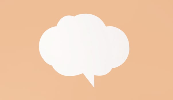 White paper speech bubble sits on peach background. The bubble is shaped like cloud and has single tail pointing downwards. It is a simple, clean image that could be used for a variety of purposes photo
