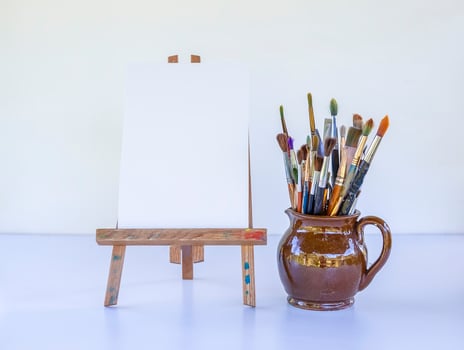 Artist's workplace. Canvas on the wooden easel and brushes in ceramic jug. photo