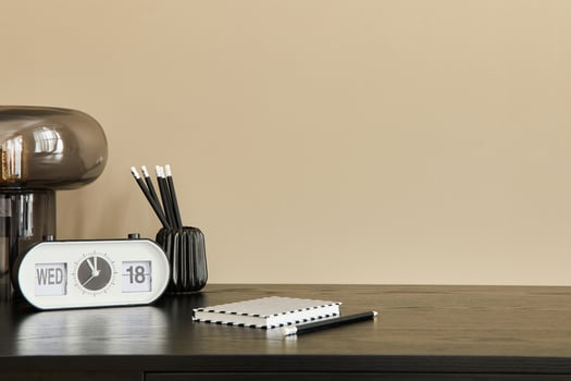 Stylish composition of office interior with black desk, table lamp, white clock, notebook and desk organizer. Template. Beige wall. Copy space. photo