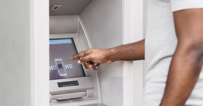 A man uses an ATM machine, pointing his finger at the screen. photo