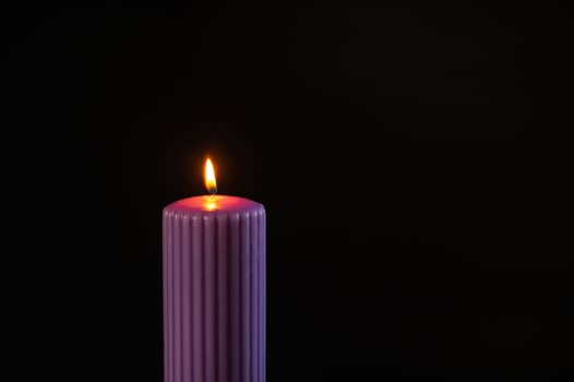Burning purple candle with orange flame over black background photo