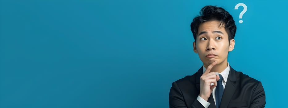 Asian Businessman in Modern Costume Pondering with Question Mark on Blue Background photo