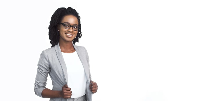 Self-assured African American businesswoman in a grey suit jacket and spectacles, standing against a white backdrop, with panoramic space for text. photo
