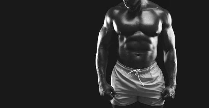 A muscular man poses in white shorts against a black background. photo