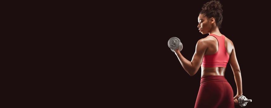 Black fitness lady doing workout with dumbbells, back view, black studio background, panorama with copy space photo
