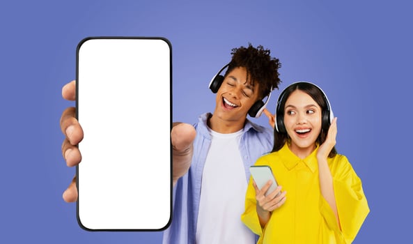 A young black man in a white shirt is standing behind her, listening to music with headphones, and holding a smartphone with a blank screen photo
