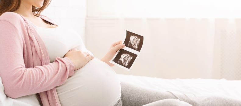 Concept of pregnancy and health care. Young mother waiting for baby, enjoying sonogram in bed, panorama with empty space photo