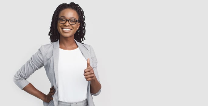 Self-confident African American corporate woman dressed in a grey blazer showing thumb up, isolated on a white background, with copy space for text. photo