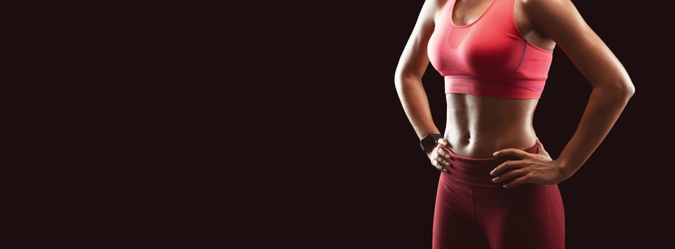Cropped of fit young african woman standing with her hands on hips over black studio background. Fitness model posing to camera. Panorama with free space photo