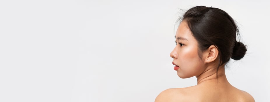Naked korean lady posing on white studio background, back view of topless asian woman looking at copy space, panorama. Woman sensuality concept photo