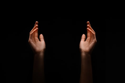This image shows two hands reaching upward in the dark. The hands are positioned symmetrically, with their palms facing upwards. photo
