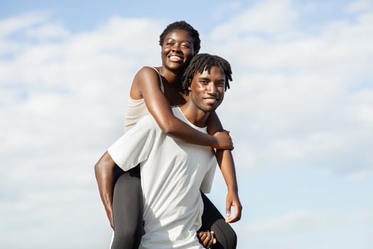 Happy black couple enjoying a piggyback ride on a sunny day. The woman is sitting on the mans back, and they are both smiling and looking at the camera. photo
