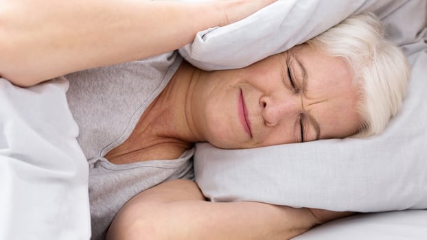 Upset senior woman closing her ears with pillow, hiding from annoying noise early in morning, panorama photo