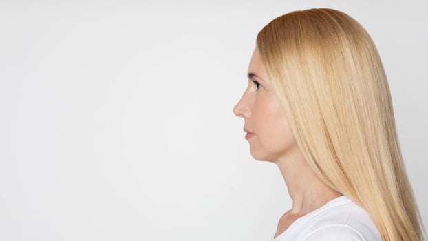 A photo of a woman with long, straight, blonde hair, looking to the right against a white background. She is wearing a white shirt, copy space
