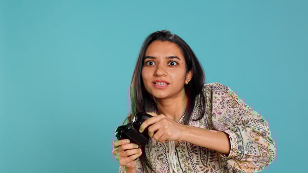 Jolly gamer celebrating after winning game on gaming console, studio background. Delighted Indian woman bragging after being victorious in videogame, defeating all enemies using gamepad, camera B photo
