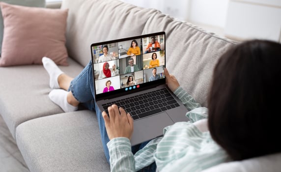 A woman relaxes on a couch, comfortably participating in a conference on her laptop. The laptop screen displays multiple participants, indicating a group meeting or discussion. photo
