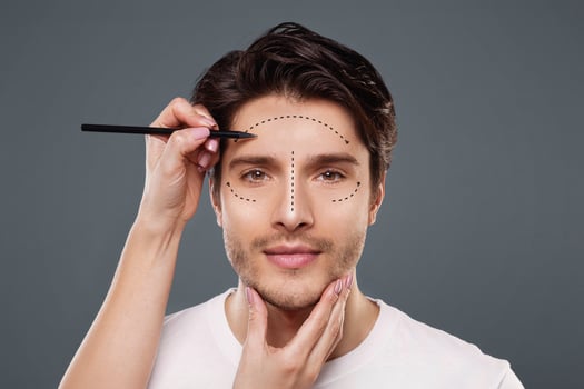 Plastic surgery concept. Surgeon drawing marks on male face on gray background, panorama photo