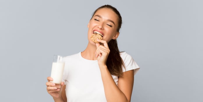 Millennial Girl Drinking Glass Of Milk And Eating Cookies Standing Over Gray Studio Background. Panorama photo