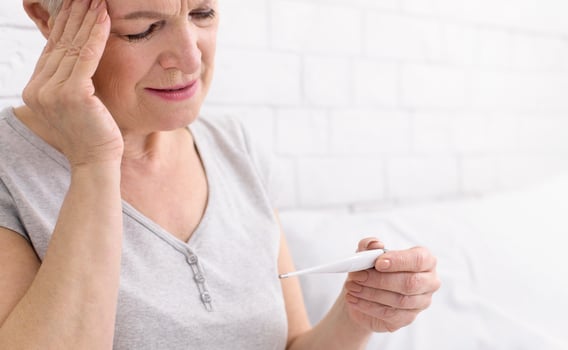 Senior woman is seen holding a thermometer in her hand, likely checking her temperature for any signs of fever or illness, closeup photo