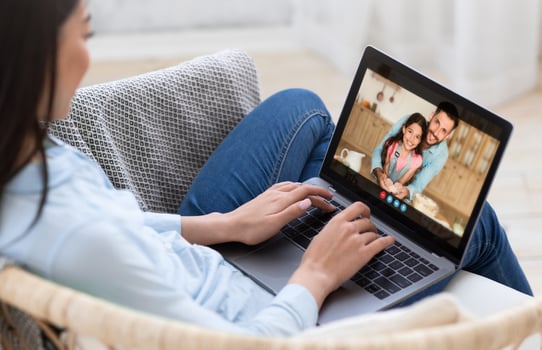 Lady sits on a couch in her living room, using a laptop to chat with her family. She appears to be smiling and happy, enjoying the connection with her loved ones. photo