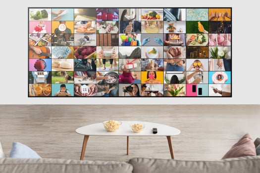 A large screen displays a collage of various everyday moments, capturing peoples activities, objects, and celebrations. The screen is mounted on a white wall in a modern living room photo