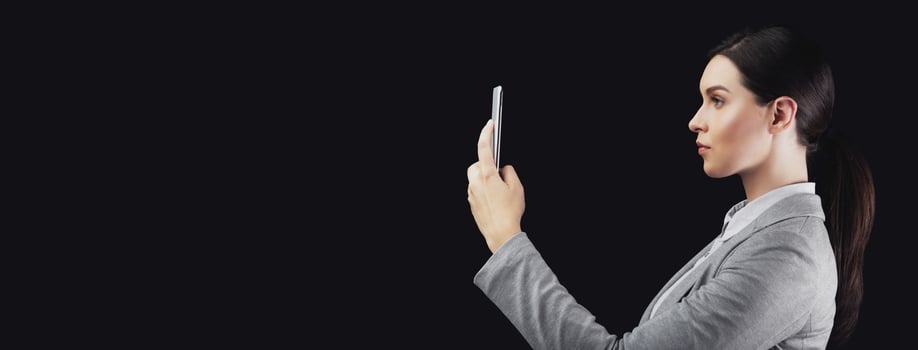 Biometric Verification. Businesswoman Holding Smartphone Using Face ID Recognition System Over Black Studio Background. Side View photo