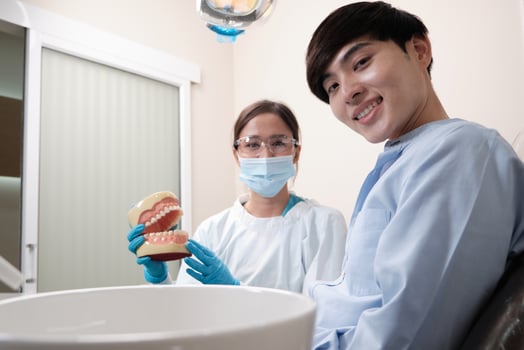 Asian female dentist explaining orthodontic care and whitening to young male patient with teeth model in dental clinic, well-being hygiene, and professional healthcare work in doctor office hospital. photo