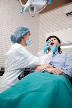 Asian female dentist examine young male patient teeth and toothache stomatology in dental clinic, well-being hygiene checks, and professional orthodontic healthcare work in doctor's office hospital. photo