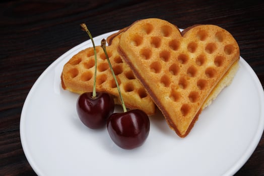 Viennese waffles with cherries lie on a white plate. Viennese waffles in the shape of a heart. photo