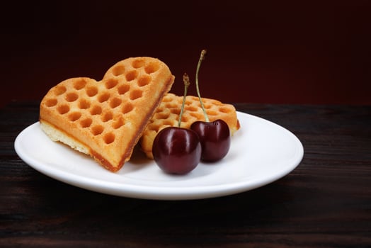 Viennese waffles with cherries lie on a white plate. Viennese waffles in the shape of a heart. photo