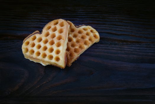 Two heart-shaped Viennese waffles lie on a dark wooden board. photo