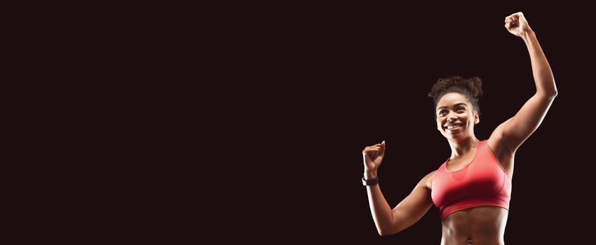 New sport achievements. Cheerful fitness african model raising her hands up, celebrating success over black, copy space photo
