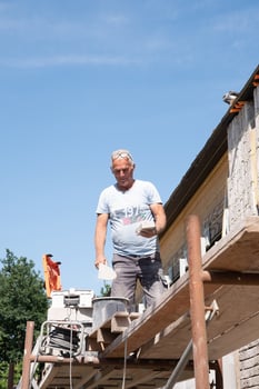 Worker applying cement mortar on brick and laying stone wall facade with trowel, outdoor construction scene on sunny day, Construction and masonry work concept, photo