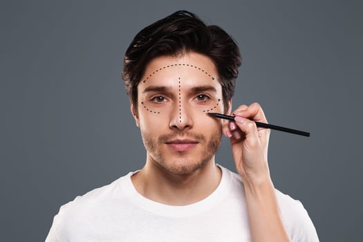 Aesthetic cosmetology concept. Surgeon drawing marks with pencil on male face on gray background, panorama photo