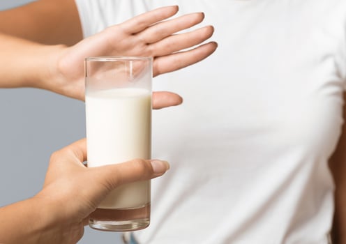 Unrecognizable Woman Gesturing No To Offered Glass Of Milk Standing In Studio On Gray Background. Cropped, Selective Focus photo