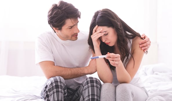 Couple dreaming to be parents. Upset man comforting his depressed wife with negative pregnancy test, free space photo