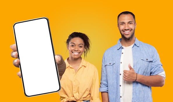 A young black woman and man are smiling and looking at the camera, the woman is holding a smartphone with a white screen and the man is giving a thumbs up. photo