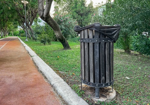 Photo of a public wooden trash bin on a path in a park.