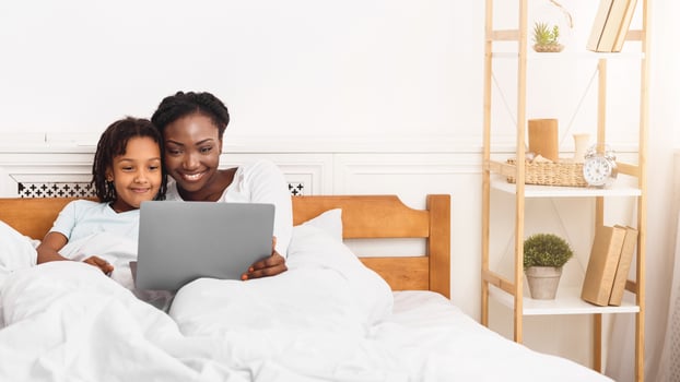 Happy Loving Family. Black mom and daughter watching on laptop, lying in bed together. Copy space, panorama photo