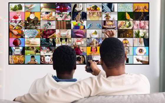 Two men are sitting on a couch and watching television. The television screen is showing a mosaic of various images, depicting different scenes and activities. photo