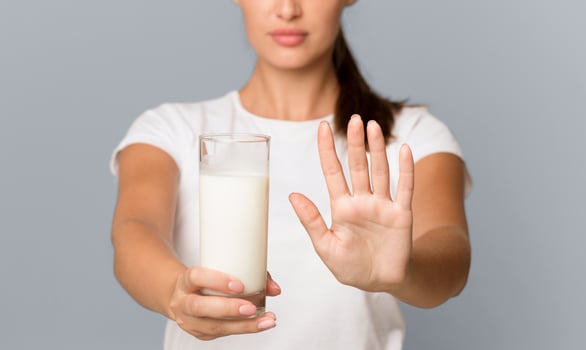 Lactose Intolerance. Unrecognizable Lady Holding Milk Gesturing No To Glass Standing Over Gray Studio Background. Cropped, Shallow Depth photo