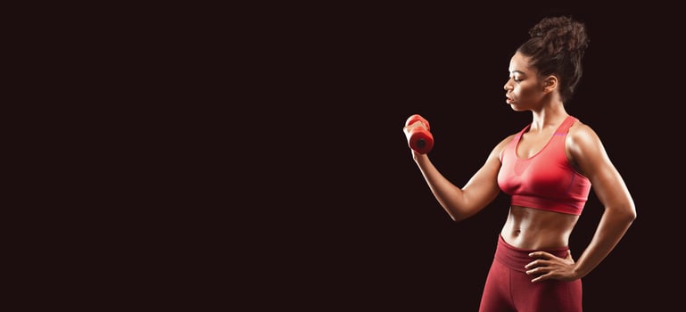 Motivated athletic afro girl working out with fitness dumbbell over black background, free space photo