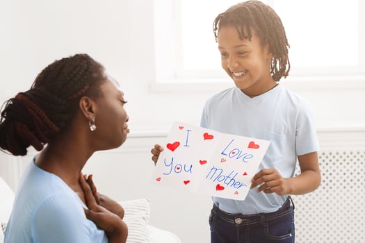 Touching Moment. African kid showing greeting card with I Love You, Mother text to her mom photo