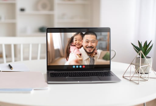 A laptop computer sits on a white table in a well-lit room. The screen displays a call of a man and a young girl, both smiling. photo