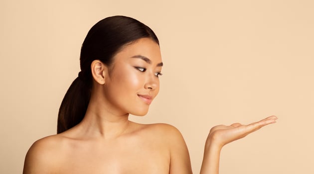 Beautiful Asian woman with long dark hair. She is wearing minimal makeup and has a natural, fresh look. The woman is looking at copy space and holding out her open hand photo