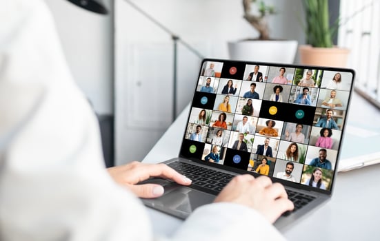 Woman sitting at a desk, actively engaged with a laptop screen displaying a group of people in a call. The individual appears focused on the virtual meeting photo