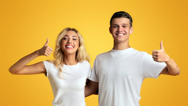 Recommended. Happy young couple showing thumbs up over yellow background, copy space photo